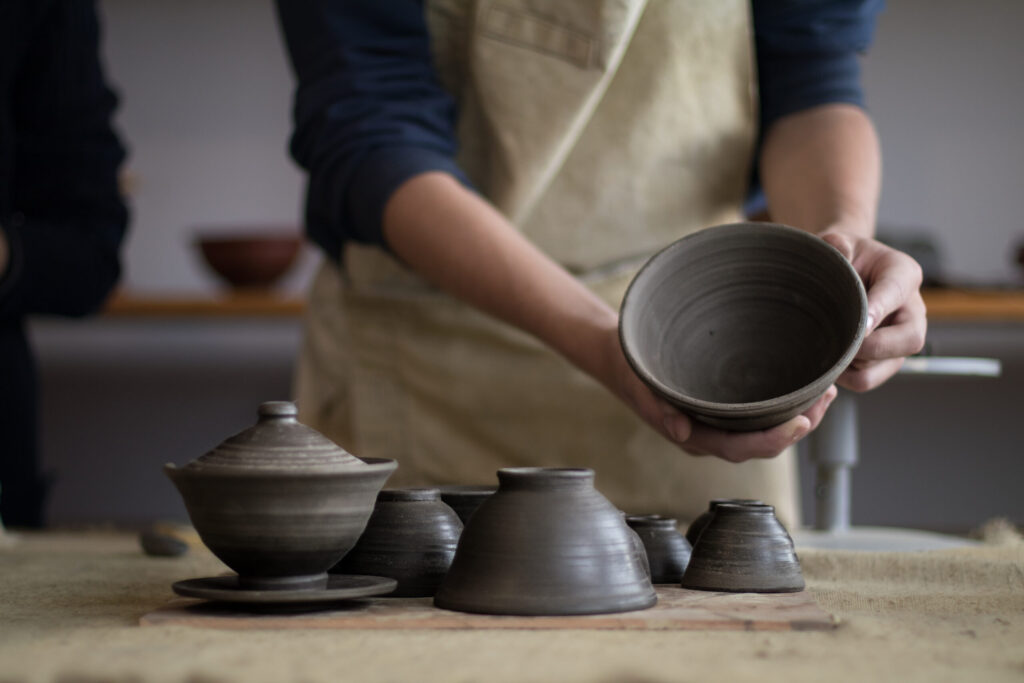Young potter dirty in clay hands holding a ceramic mug that he made