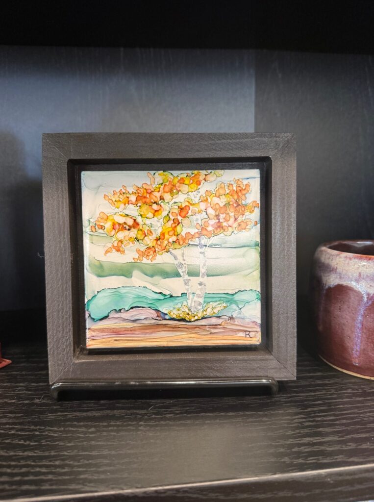 Framed painting of a tree with orange foliage displayed in the House of Clay gallery.