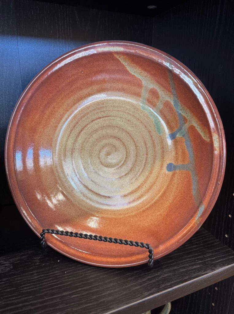 Handmade ceramic plate with spiral center and orange glaze displayed in the House of Clay gallery.