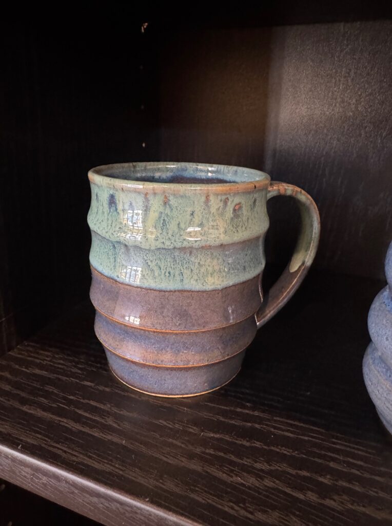 Handmade ceramic mug with layered blue and green glazes displayed in the House of Clay gallery.